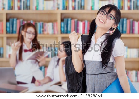 Photo of excited female high school student with her group in the library