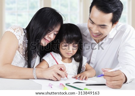 Image of two happy asian parents help their daughter learn and write on the book, shot at home