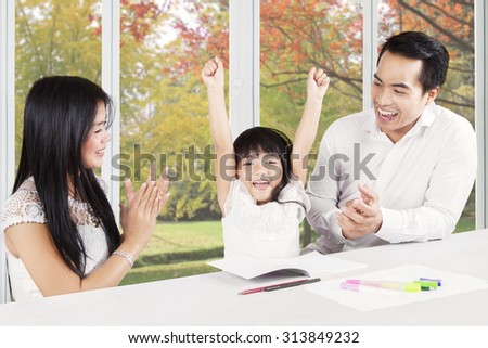 Image of two young hispanic parents giving applause on their child at home after finishing homework