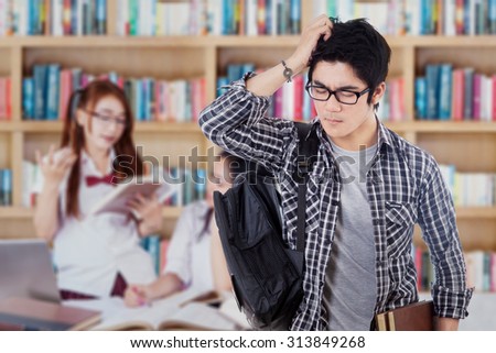 Image of confused high school student standing in the library with his group studying on the back