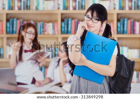 Image of a beautiful female student standing in the library with her group studying on the back