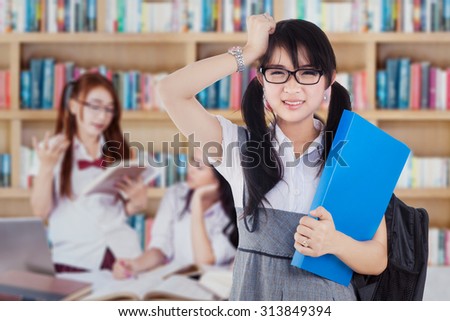 Image of confused high school student standing in the library with a group of student studying on the back