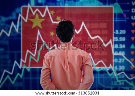 Young male broker looking at a stock market of china with declining arrows