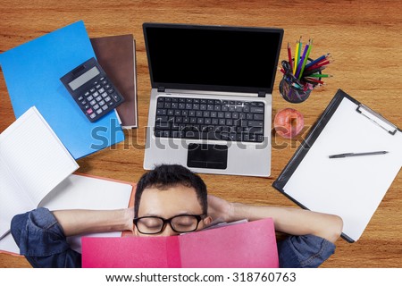 Image of male high school student sleeping on the floor with laptop, books, and stationery