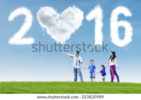 Image of happy family walking on the meadow with cloud shaped numbers 2016