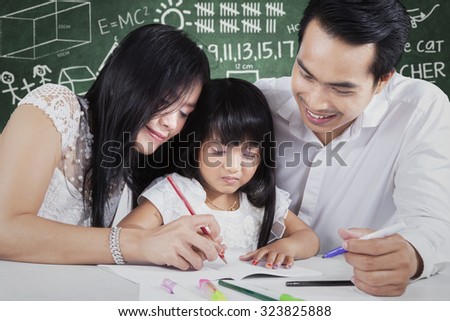 Photo of two young asian teacher teach a female elementary school student studying and write on the book, shot in the classroom