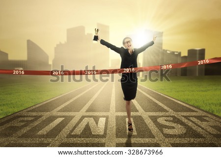 Photo of young business woman winning the race competition and crossing the finish line while carrying a trophy
