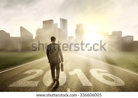 Image of male entrepreneur walking on the road with numbers 2016 while carrying suitcase