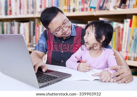 Photo of friendly male teacher talking with female student in the library while teaching her