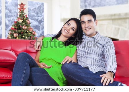 Portrait of happy young couple smiling at the camera while sitting on the sofa at home with a christmas tree background