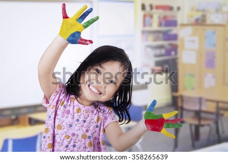 Smiling little girl with hands painted in colorful paints on classroom