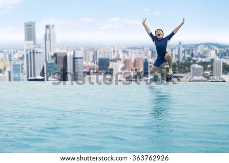 Happy little boy jumping into an infinity swimming pool at sunny day