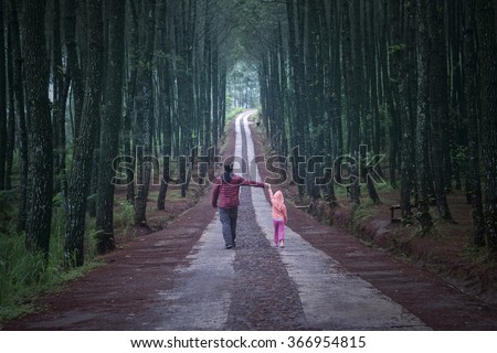 Young man walking in the pine forest while holding hands with his daughter