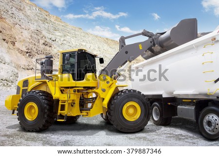 Image of a yellow backhoe loading a mine with a scoop into the truck at mining site