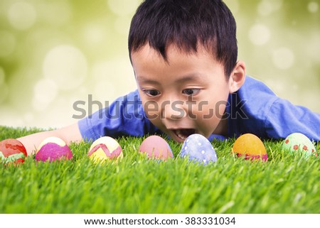 Portrait of surprised little boy lying on the grass and finding easter eggs, shot with bokeh background