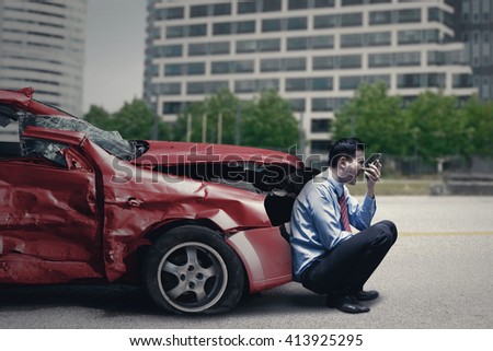 Angry person speaking on the cellphone while sitting in front of a broken car after traffic accident