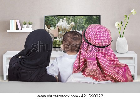 Arabian family sitting on the sofa while watching television together in the living room