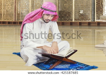 Portrait of Arabic person sitting in the mosque while reading Quran and wearing traditional clothes