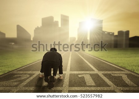 Businessman wearing a formal suit in ready position to run toward the city with numbers 2017 on the road