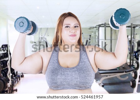 Portrait of obese woman lifting dumbbells while standing at the fitness center