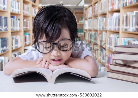 Portrait of elementary school student sitting in the library while reading textbooks on desk