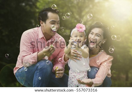 Portrait of cheerful family playing with soap bubbles while laughing together in the park