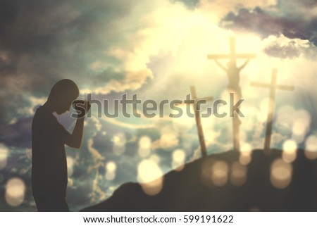 Silhouette of a young Christian man praying to God with three crucifixes in the hill