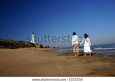 Couple at the beach holding hands walking towards the lighthouse