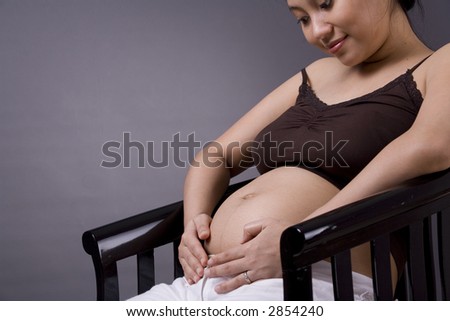 Studio shot of a pregnant woman standing over grey background with her stomach exposed