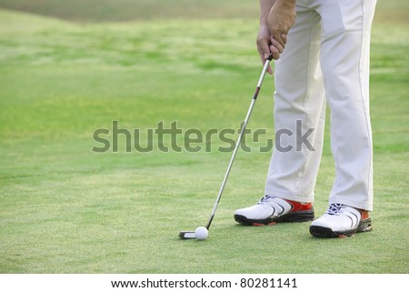 Putter behind golf ball with feet of golfer in background