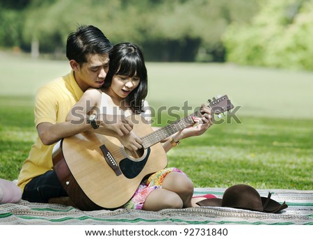 Romantic young couple playing guitar in the park