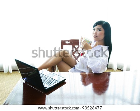Sexy Asian businesswoman with laptop and a mug of coffee