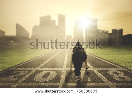 Back view of young woman ready to run toward a city while kneeling on the road with numbers 2018