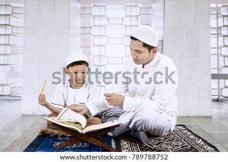 Picture of young man wearing Islamic clothes while teaching his son reads the Quran in the mosque