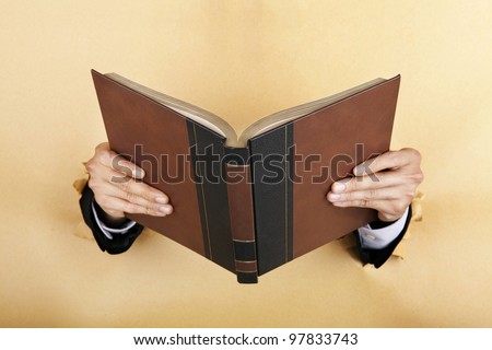 Businessman hand holding a book breaking through a paper wall