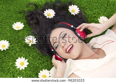 Beautiful woman listens to music while laying on the grass with flowers