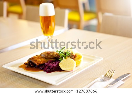 Roast duck with red cabbage and potato dumplings, in the background a restaurant out of focus