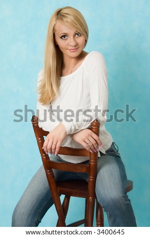 Sexy girl sits on a wooden chair. Blue background.