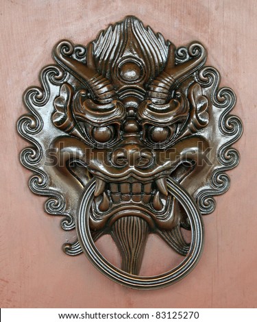 Old bronze door knocker in shape of dragon head on wooden door background.