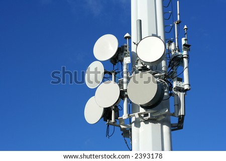 A series of microwave, satellite, and cell phone dishes against a clear blue sky.