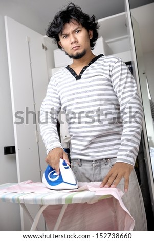 young asian man unhappy during ironing his shirt