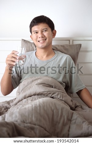 young Thai man drinking water in the morning on his bed