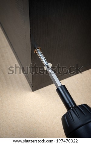 worker screws in a wooden furniture with a screwdriver