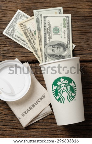 BANGKOK, THAILAND - JULY 15, 2015: White paper cup with Starbucks logo and Dollar bills. Starbucks is the world's largest coffee house with over 20,000 stores in 61 countries.