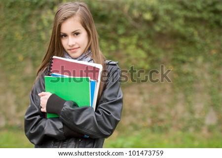 Portrait of a fresh young student girl in the park holding exercise books.