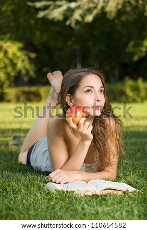Portrait of a cute young brunette student in the park having fun reading a book.