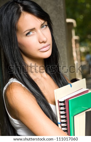 Portrait of a very tanned gorgeous young brunette student girl outdoors holding exercise books.