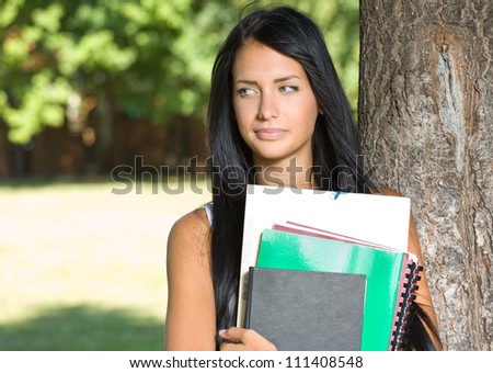 Portrait of an attractive young brunette student outdoors with exercise books.