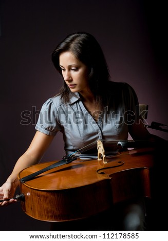 Preparing to perform, beautiful young cellist woman checking her instrument.