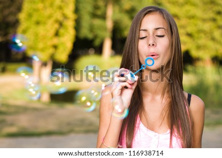 Dreamy blond teen beauty blowing soap bubbles.
